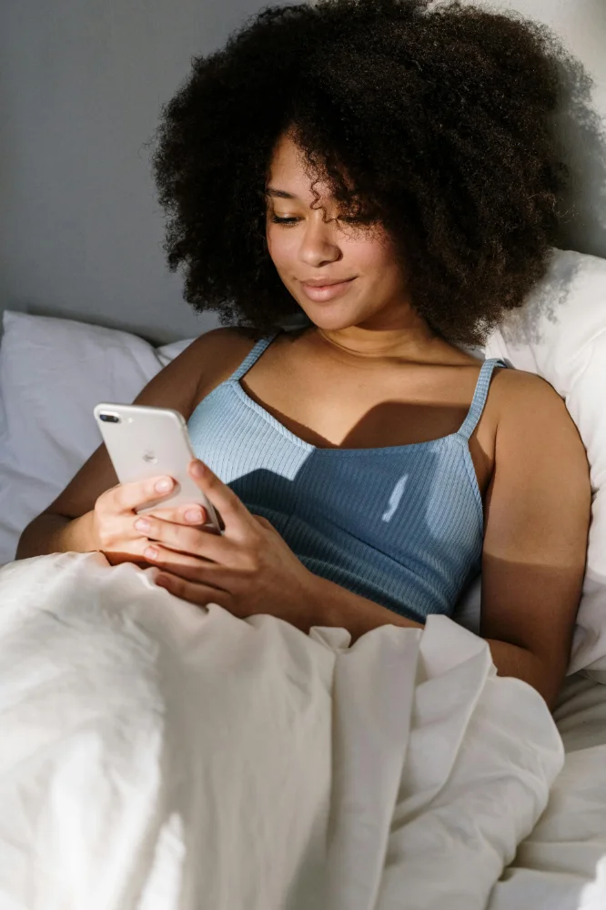 Photo of a woman on her phone in her bed.